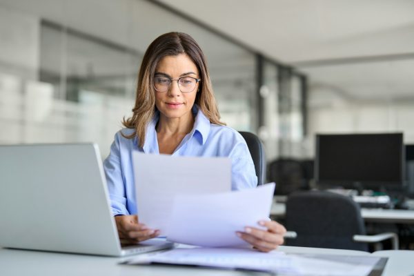 Busy business woman of middle age working on laptop checking documents.