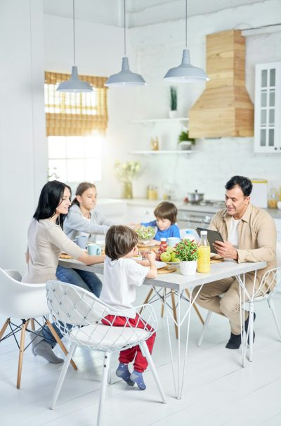 Full length shot of cheerful hispanic family enjoying meal together while having lunch, sitting at