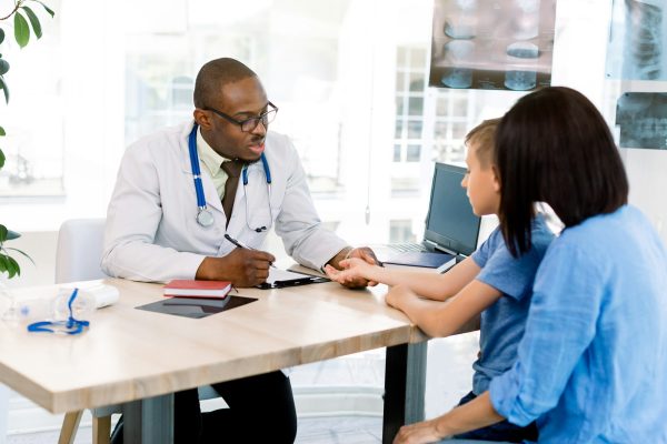 Pediatrician Meeting With Mother And Child In Hospital. Mother Taking Son For Medical Exam In